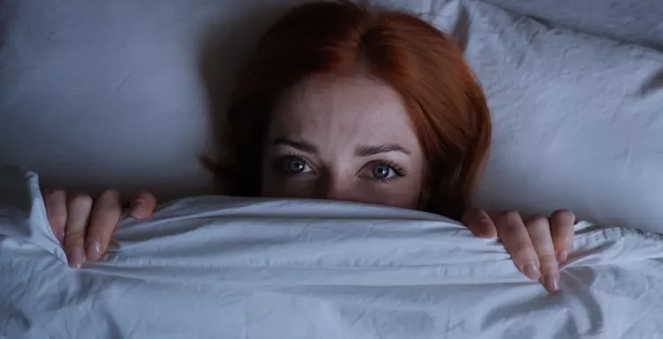 sleepless woman lying in bed hiding under duvet at night